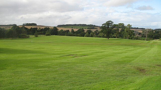 A green field with trees and hills in the background.