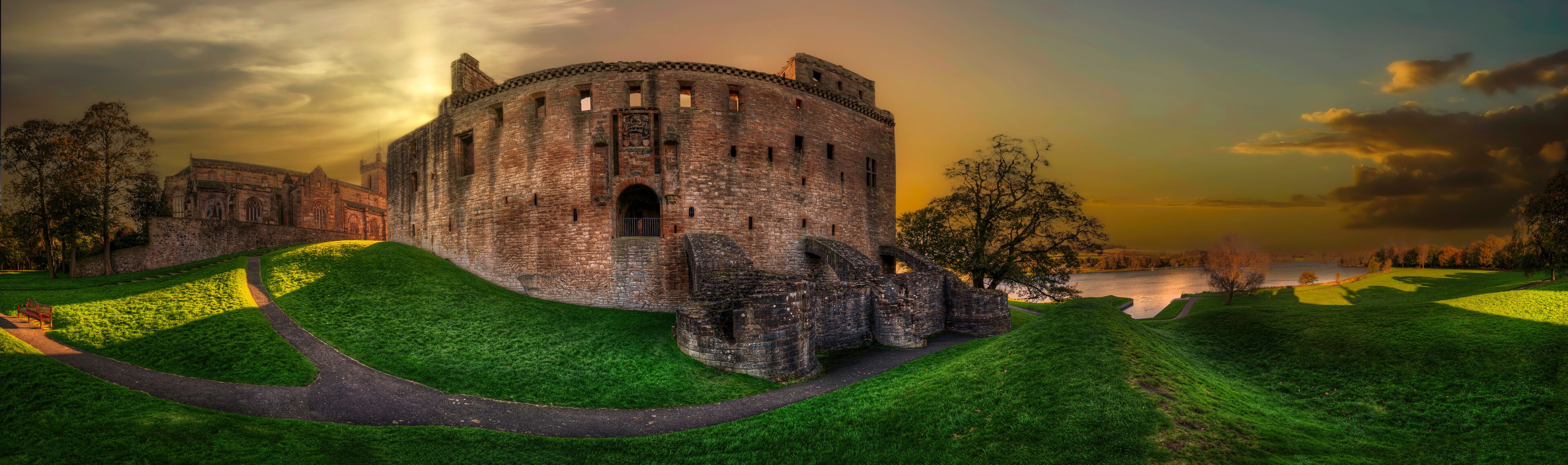 A historic castle with a moat, surrounded by lush green hills and a serene lake.