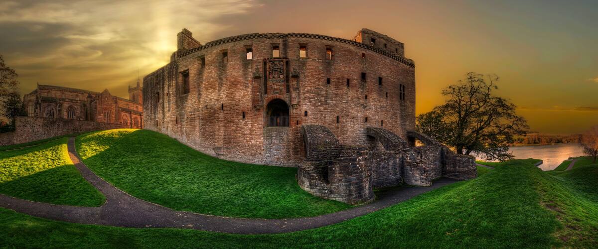 A historic castle with a moat, surrounded by lush green hills and a serene lake.