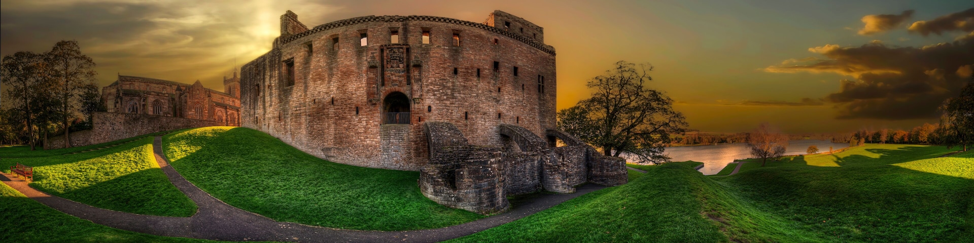 A historic castle with a moat, surrounded by lush green hills and a serene lake.