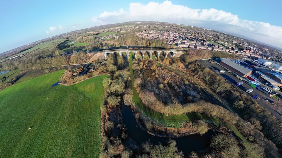 An aerial view of a town with a bridge, green fields, and a river.