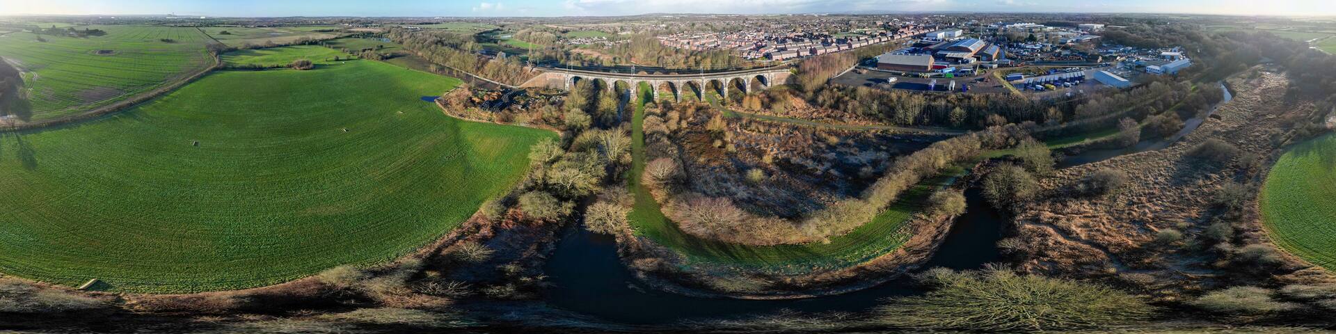 An aerial view of a town with a river, green fields, and a bridge.