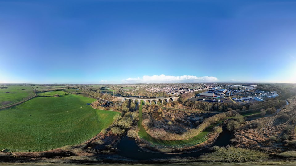 An aerial view of a town with a river, green fields, and a bridge.