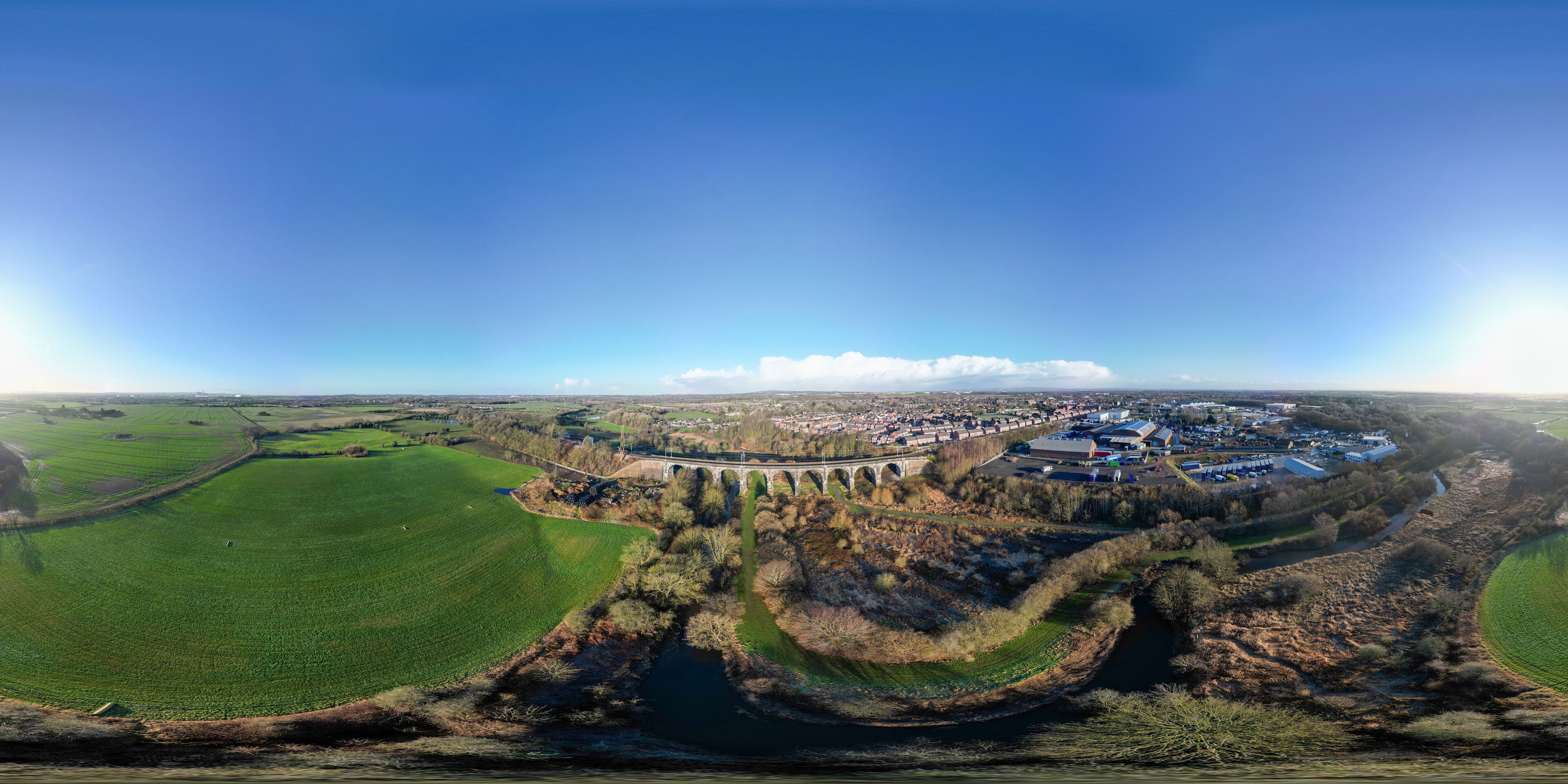 An aerial view of a town with a river, green fields, and a bridge.
