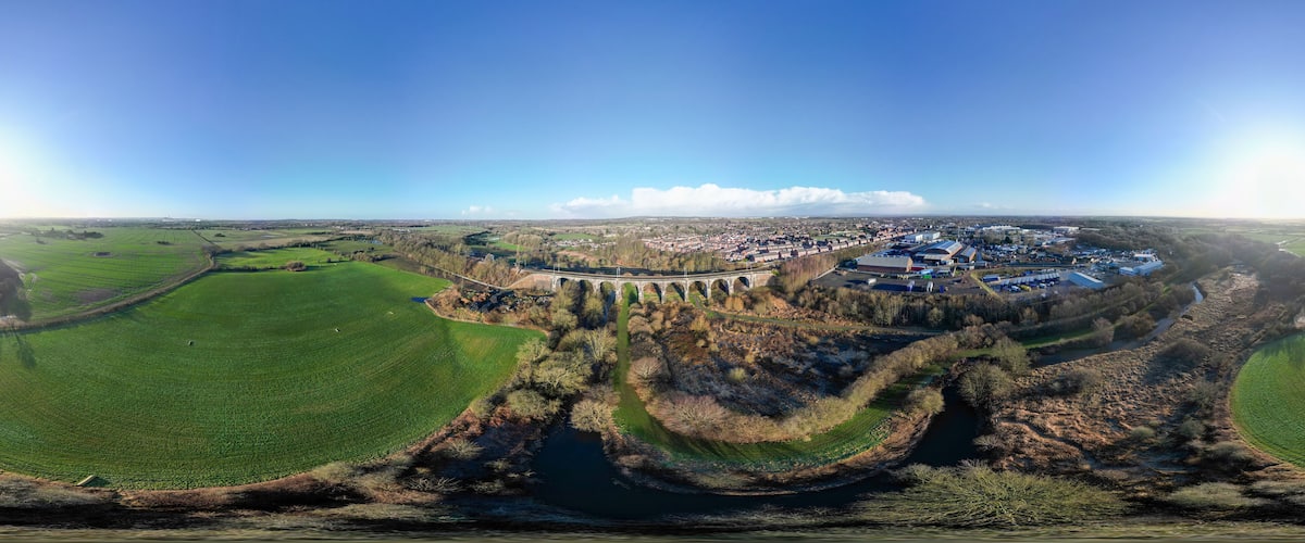 An aerial view of a town with a river, green fields, and a bridge.