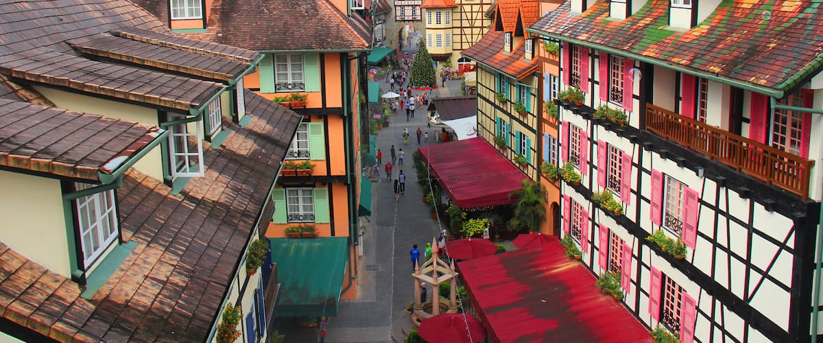 A narrow street lined with colorful half-timbered houses, a church steeple, and a mountain in the background.