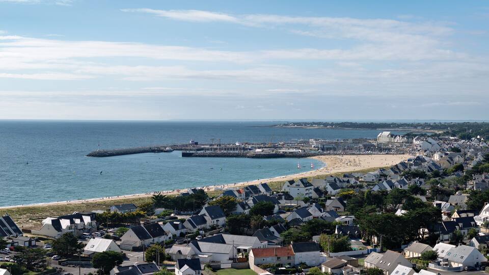 A coastal town with a beach, houses, and a pier extending into the sea.