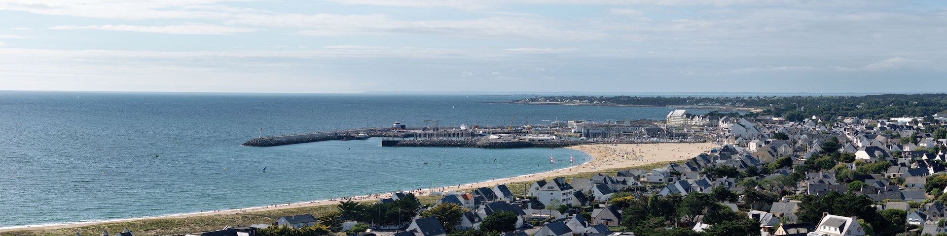 Un pueblo costero con una playa, casas y un muelle que se adentra en el mar.