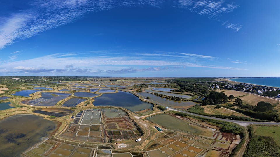 An aerial view of a coastal area with multiple water bodies, a residential zone, and a clear sky.
