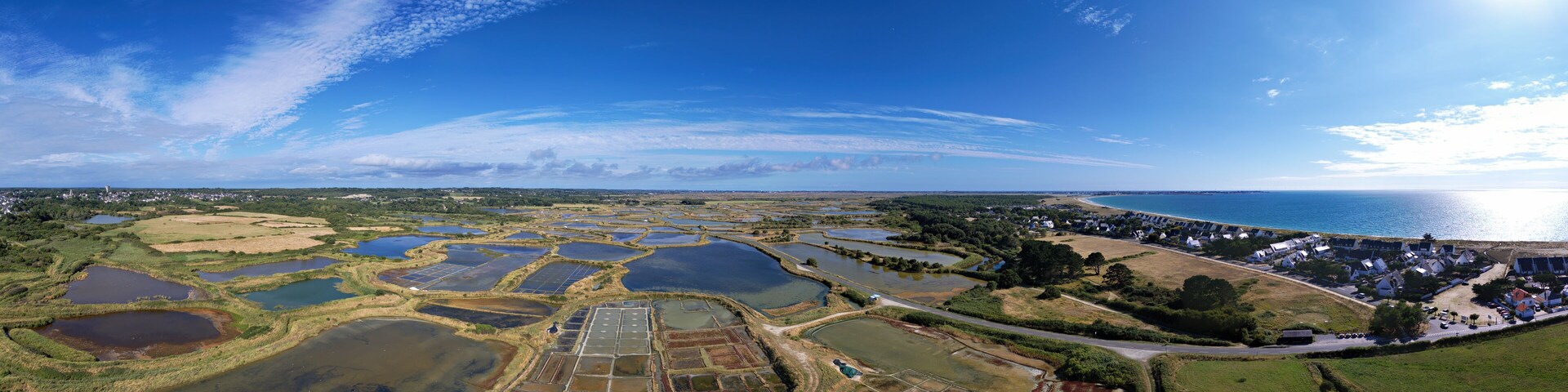 An aerial view of a coastal area with multiple water bodies, a residential zone, and a clear sky.