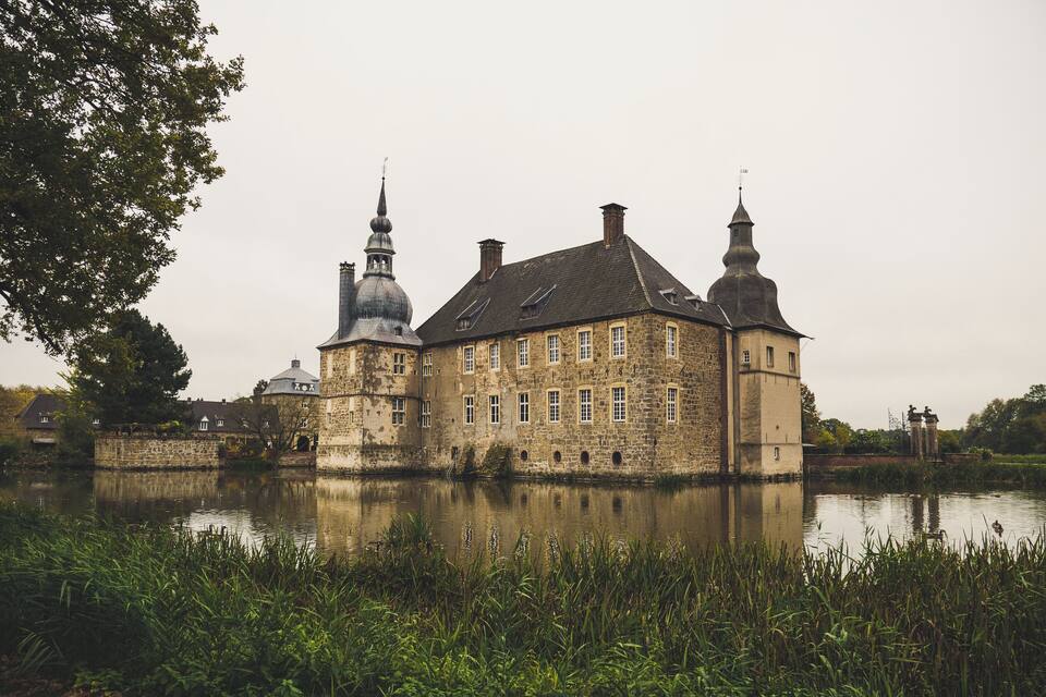 A historic stone building with multiple towers and a reflection in the water.
