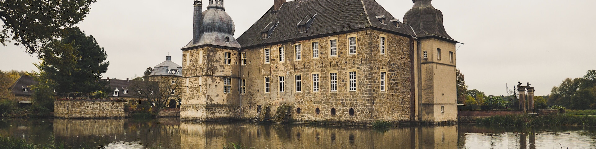 A historic stone building with multiple towers and a reflection in the water.