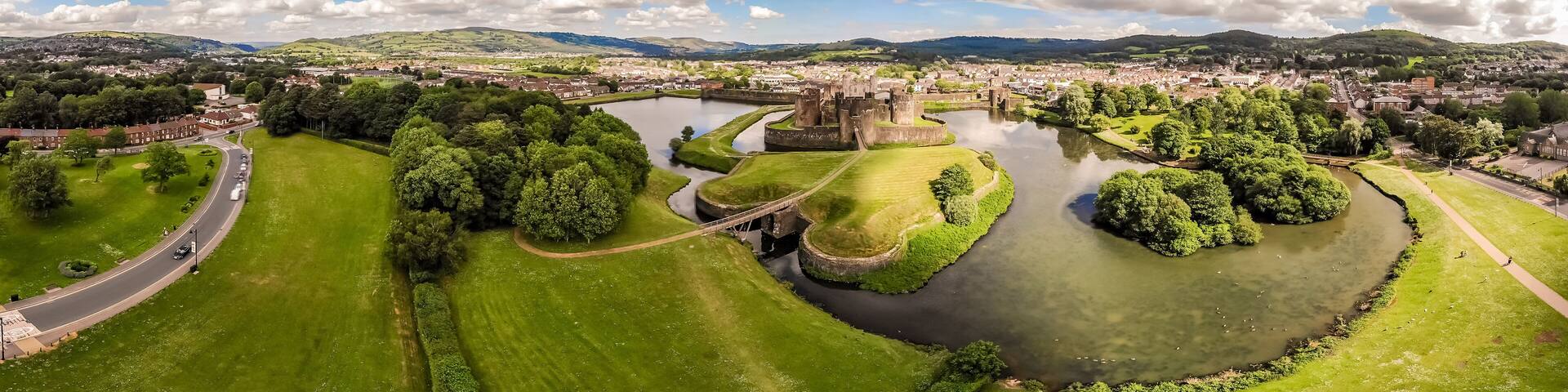 A panoramic view of a town with a river, green parks, and historic buildings.