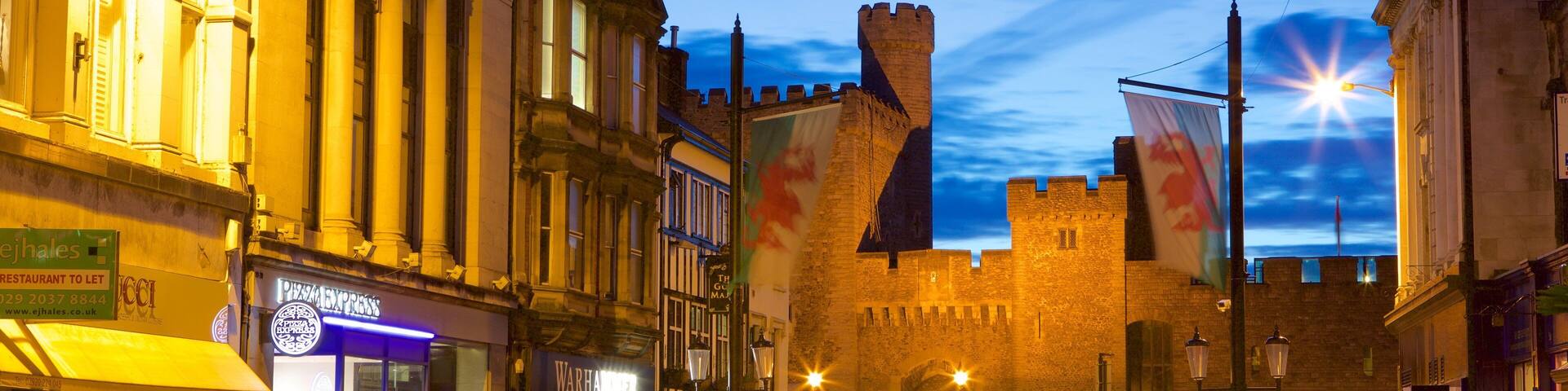 A historic castle with a moat, surrounded by modern buildings with illuminated signs.