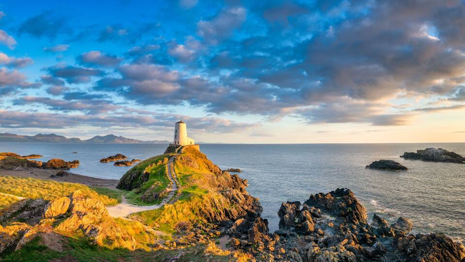 A coastal landscape with a lighthouse on a rocky outcrop, a clear sky, and calm sea.