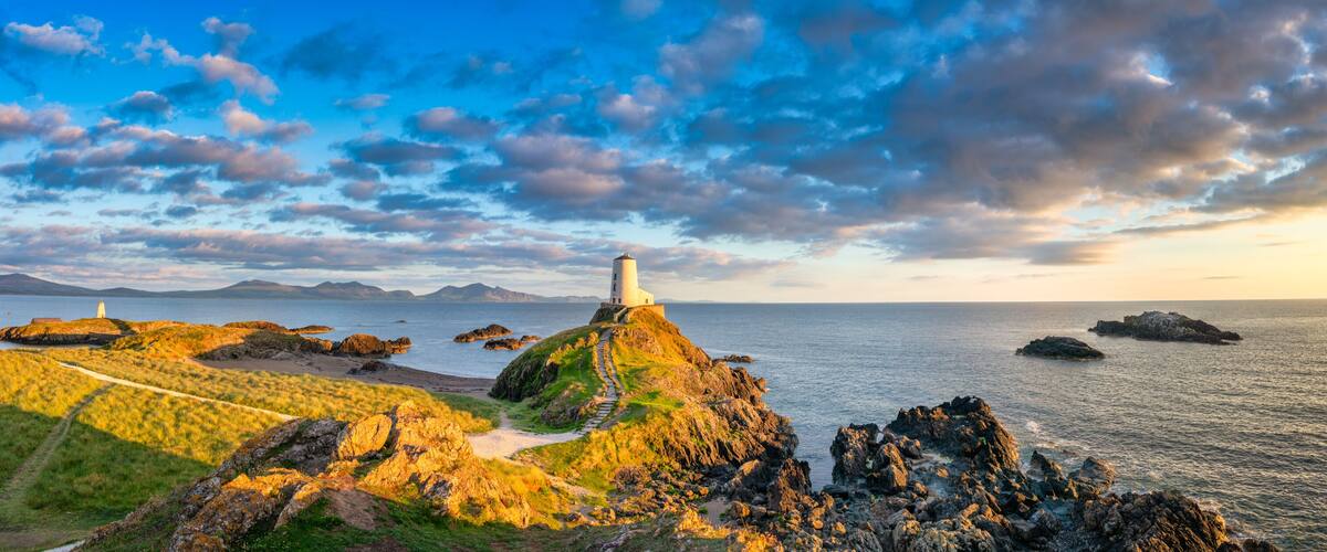 A coastal landscape with a lighthouse on a rocky outcrop, a clear sky, and calm sea.