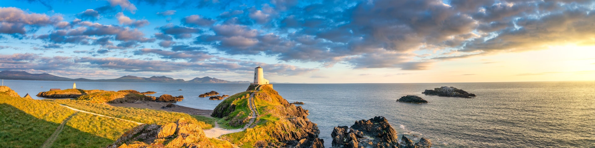 A coastal landscape with a lighthouse on a rocky outcrop, a clear sky, and calm sea.