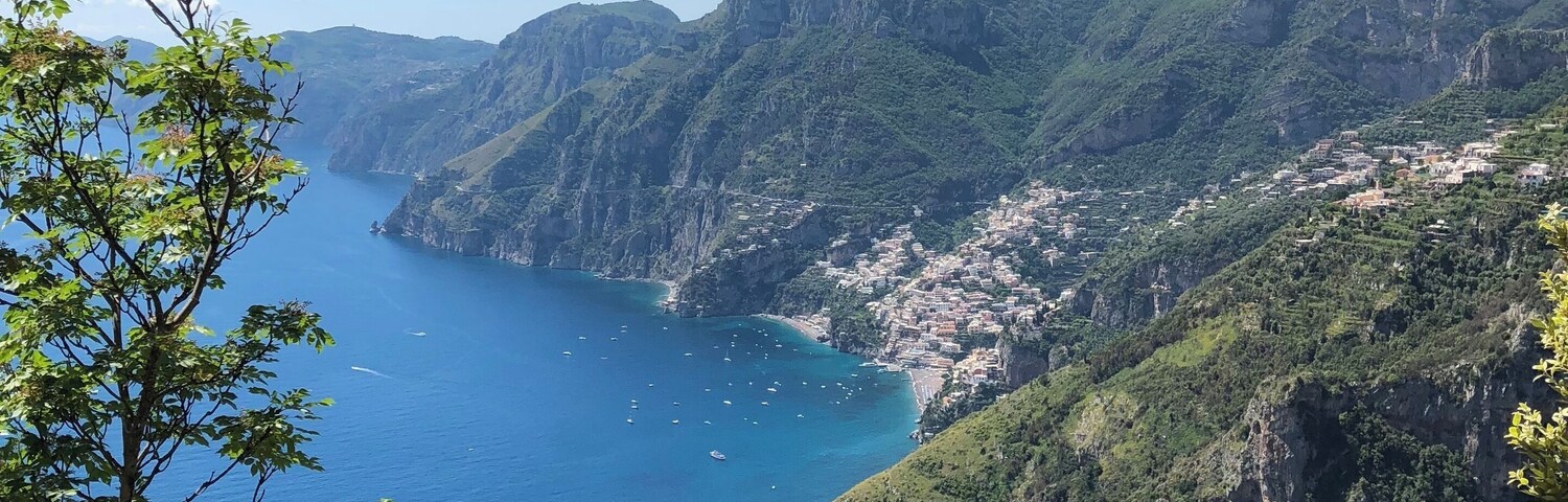 Un paisaje costero con mar azul cristalino, colinas verdes y un pueblo pequeño enclavado entre montañas.