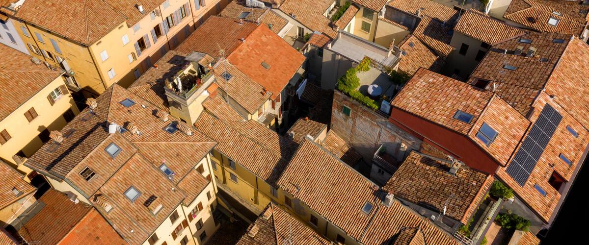 An aerial view of a densely packed urban area with terracotta-tiled rooftops and a mix of building colors.