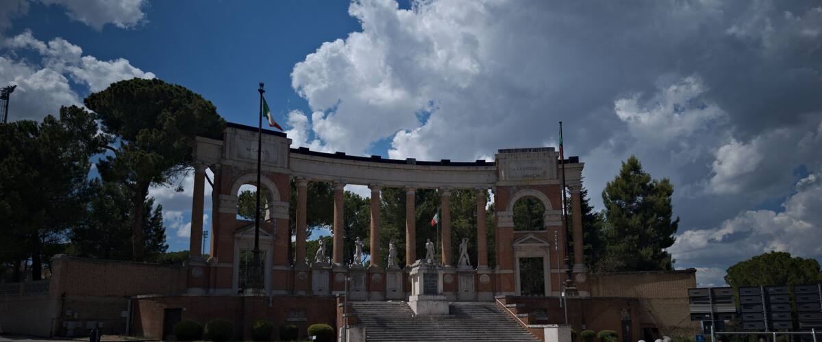 A grand archway with statues, surrounded by trees and a clear sky.