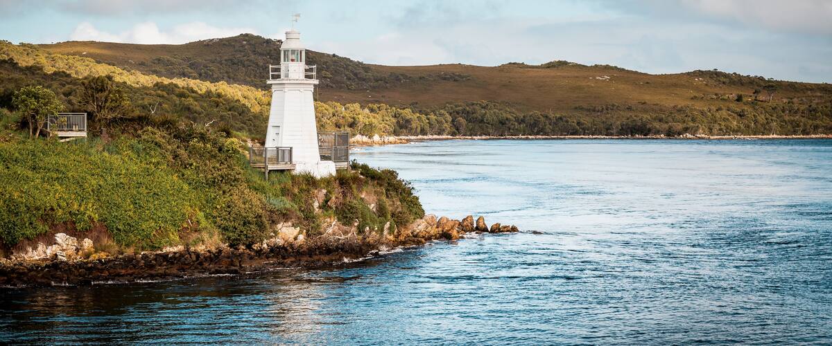 A lighthouse on a rocky shore with a clear view of the surrounding hills and calm sea.