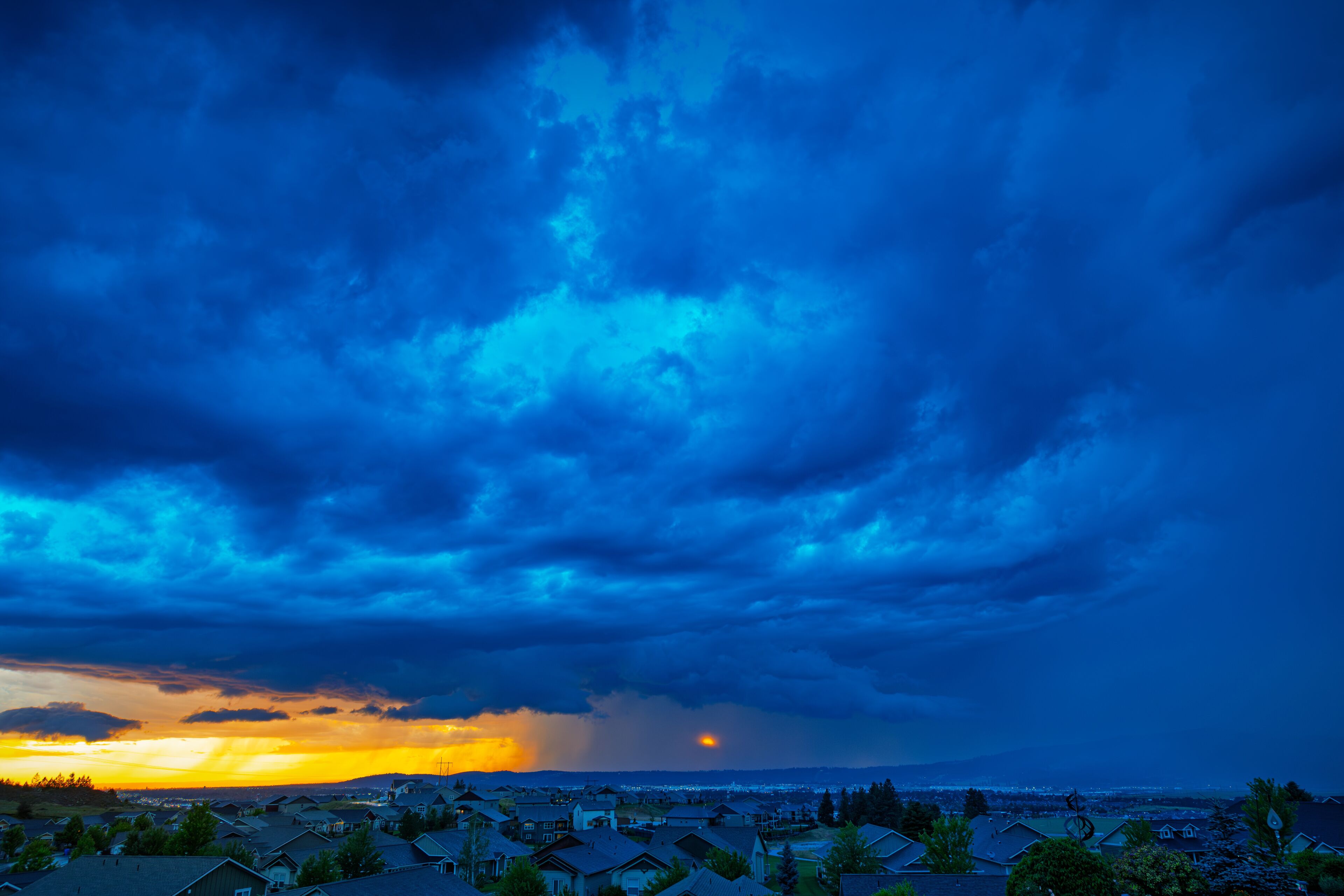 Storm clouds over the city of Spokane Washington with bright sunshine on one side, heavy rain on the other side and the sun breaking through in the center.