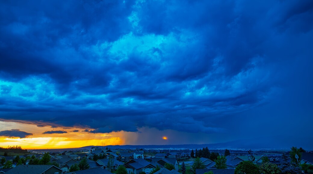 Storm clouds over the city of Spokane Washington with bright sunshine on one side, heavy rain on the other side and the sun breaking through in the center.