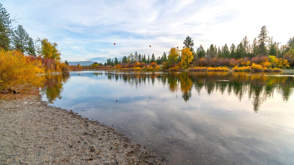 A calm river reflecting autumn trees and a clear sky.