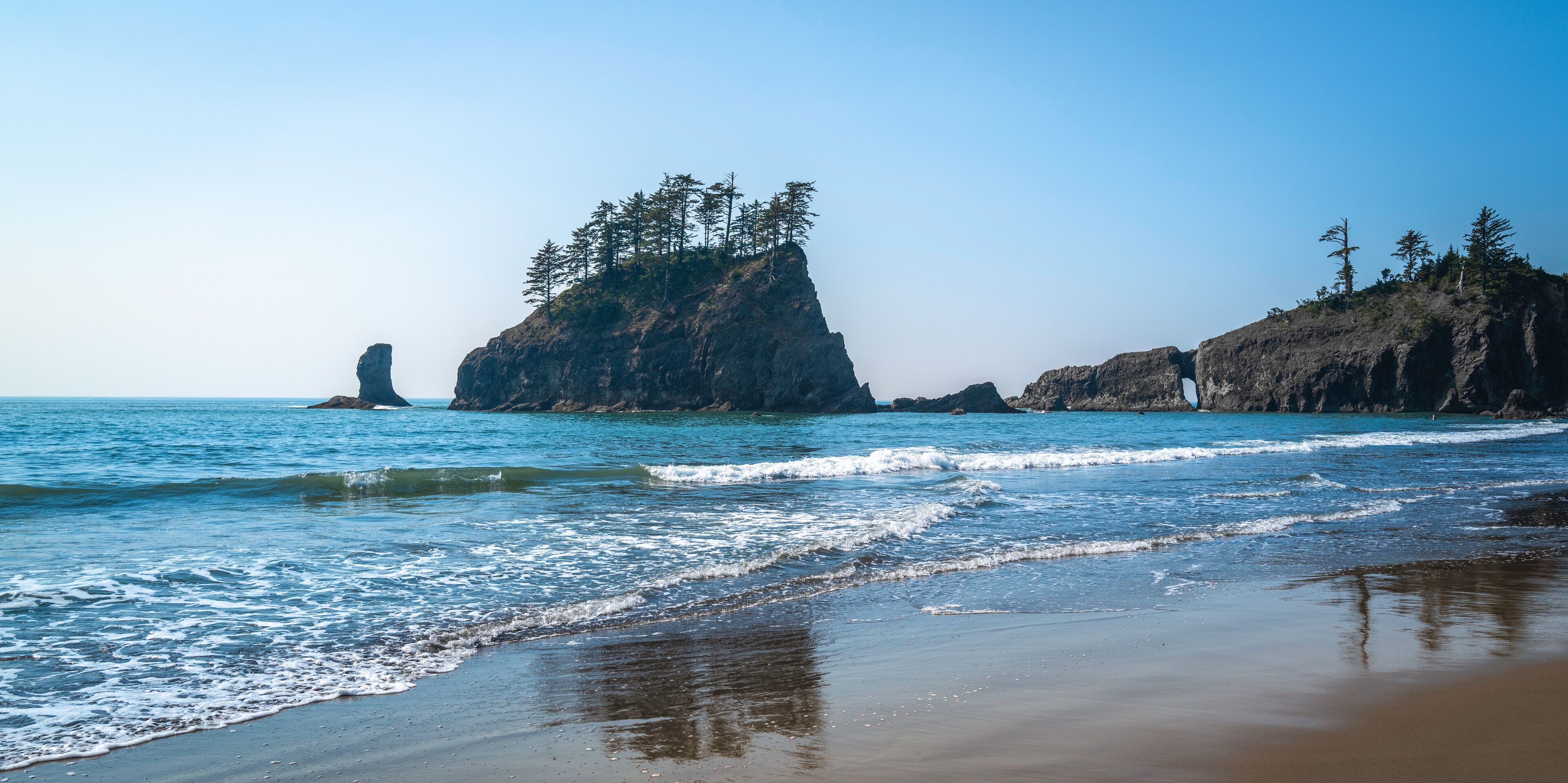 A beach with waves, rocky cliffs, and trees.
