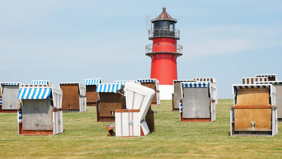 A red lighthouse and several beach huts with striped awnings.