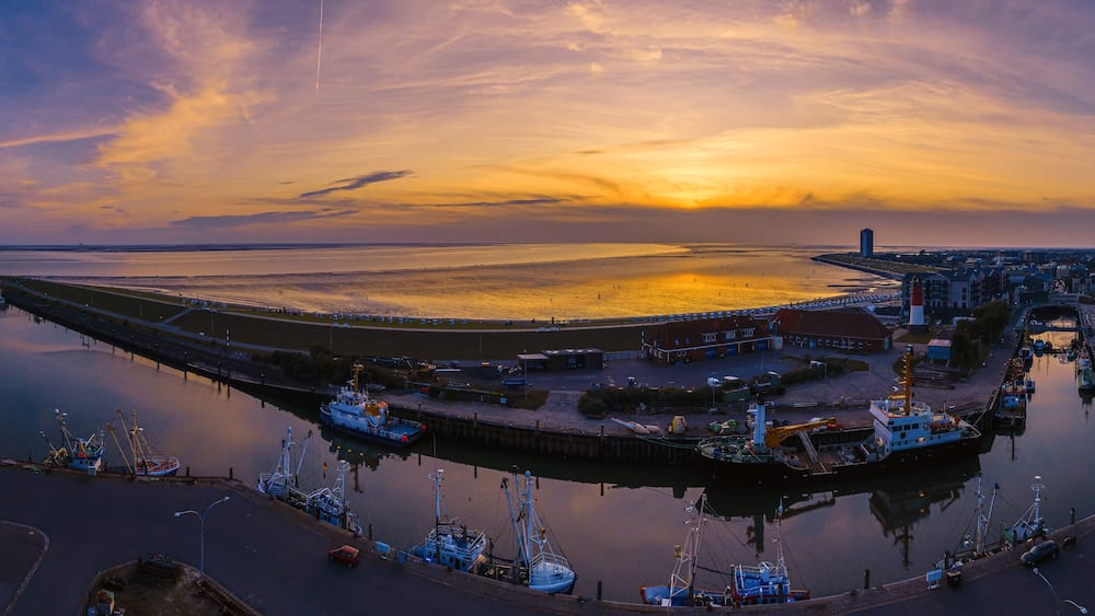 Ein Hafen im Abendrot mit Booten, einer Brücke und einer entfernten Stadtansicht.