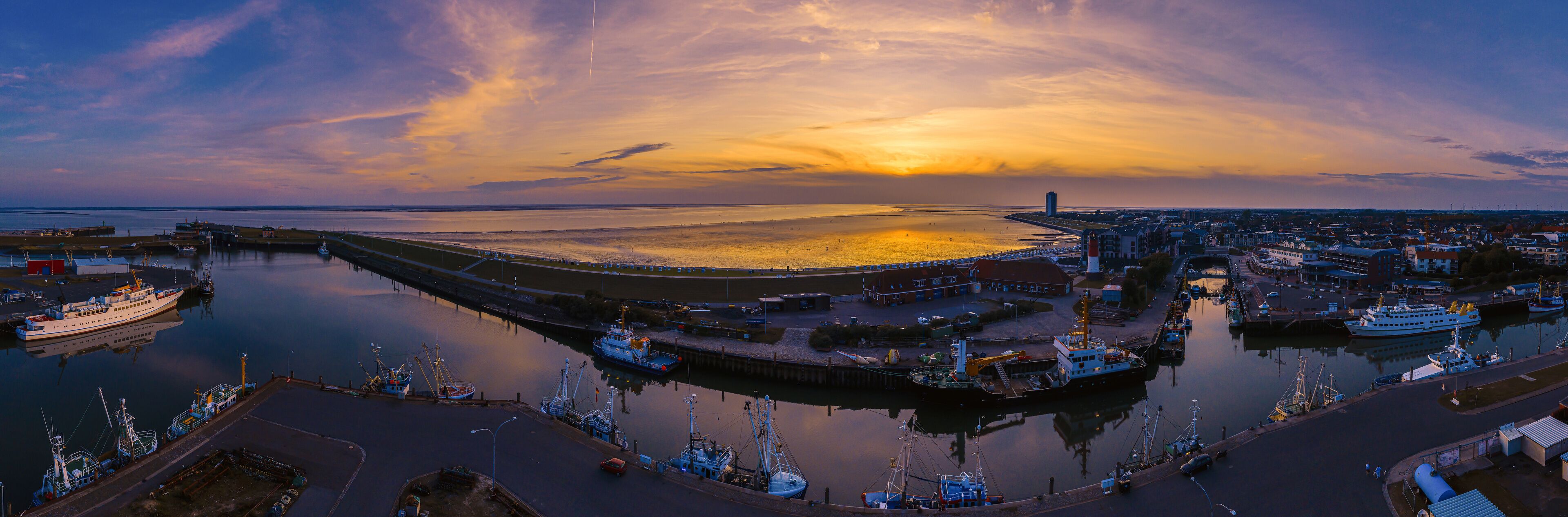 A harbor at sunset with boats, a bridge, and a distant cityscape.