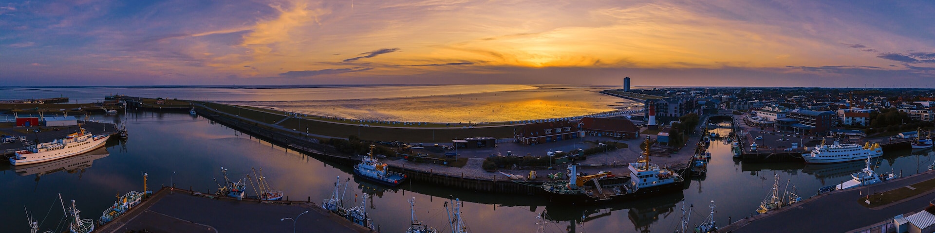 A harbor at sunset with boats, a bridge, and a distant cityscape.