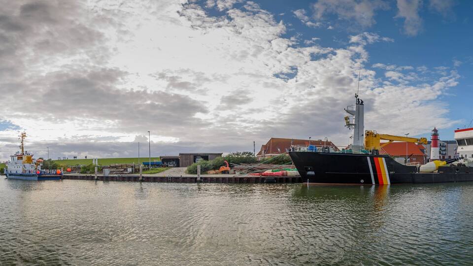 A harbor with a large ship docked, a crane, and a lighthouse in the background.