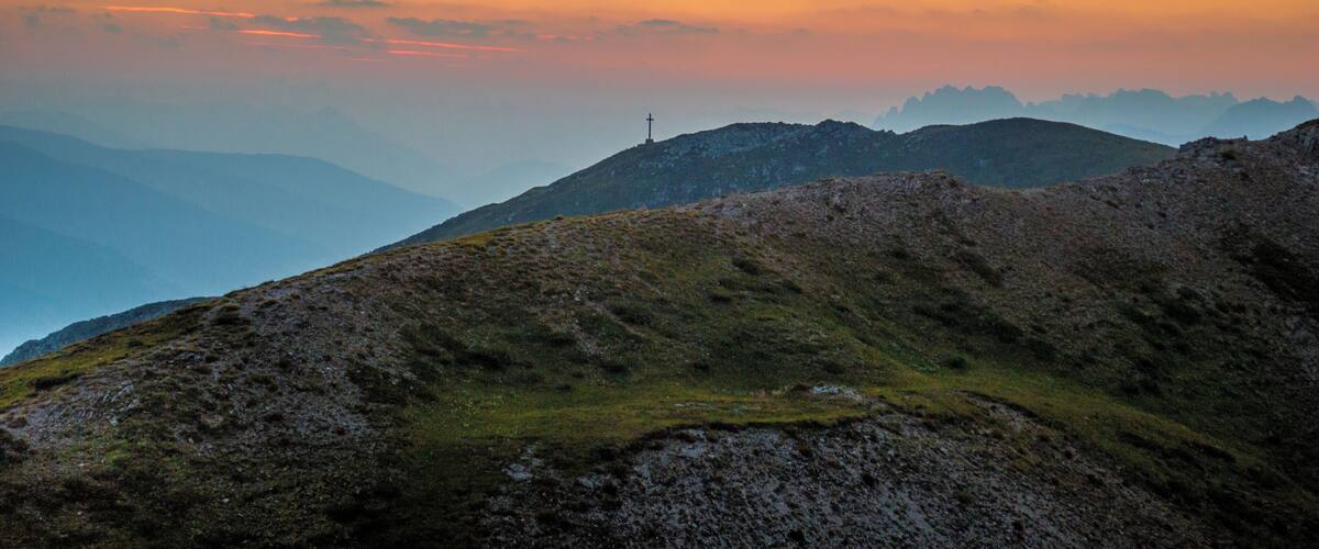 A mountain landscape with a cross on a hill during sunset.