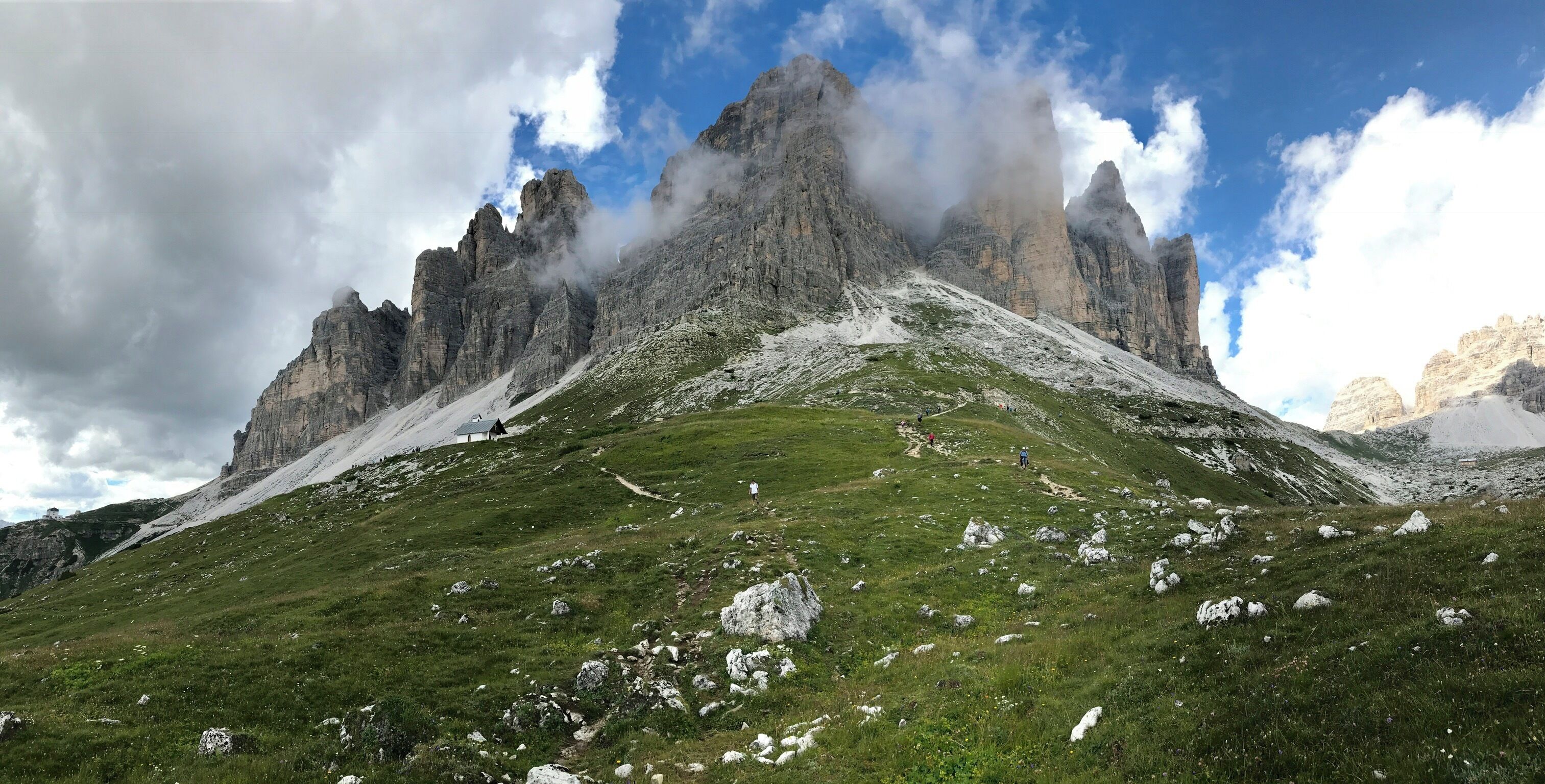 A mountain landscape with rocky peaks, a grassy slope, and a small shelter.