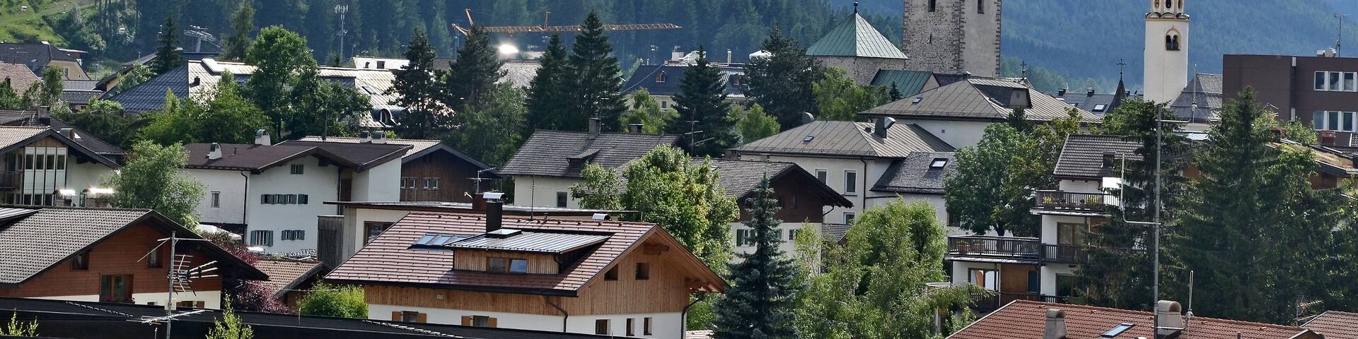 A town nestled in a valley with mountains in the background, featuring a prominent church tower and a mix of residential buildings.