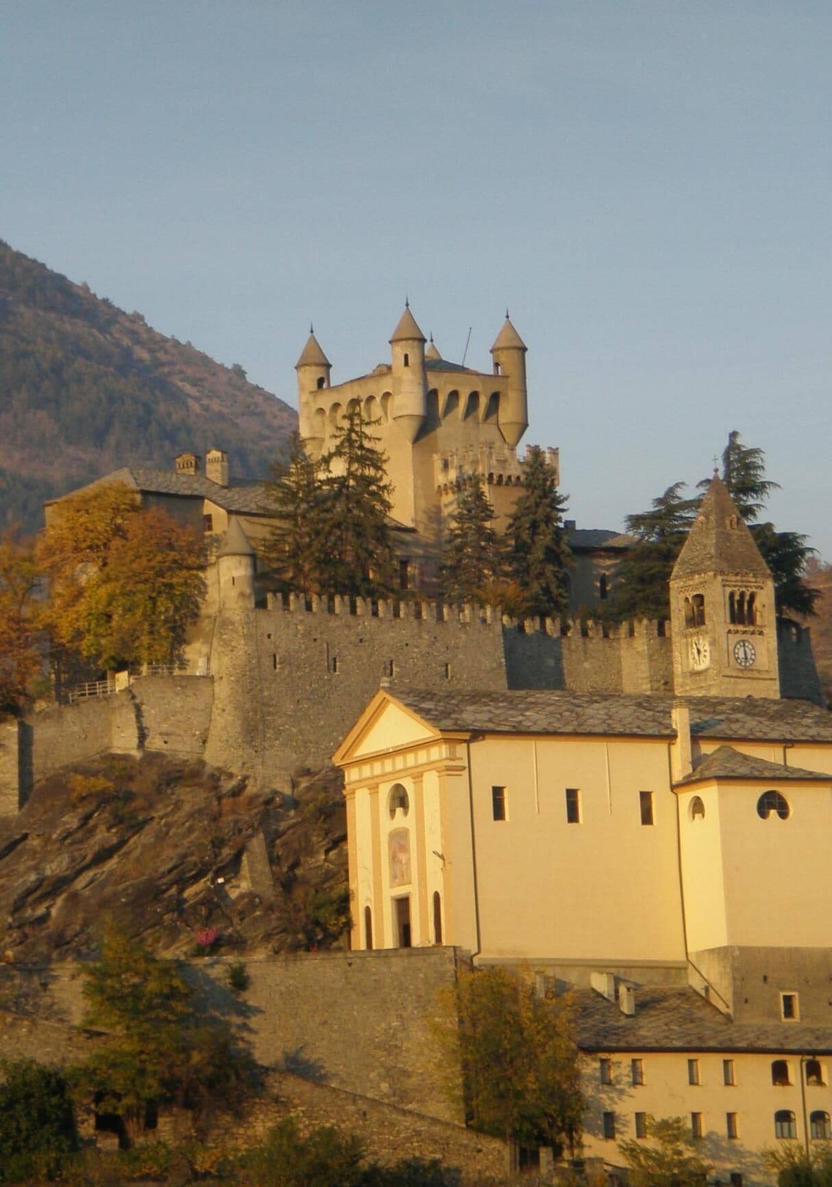 Eine Burg mit mehreren Türmen und einem Uhrturm, umgeben von Bäumen und Gebäuden.