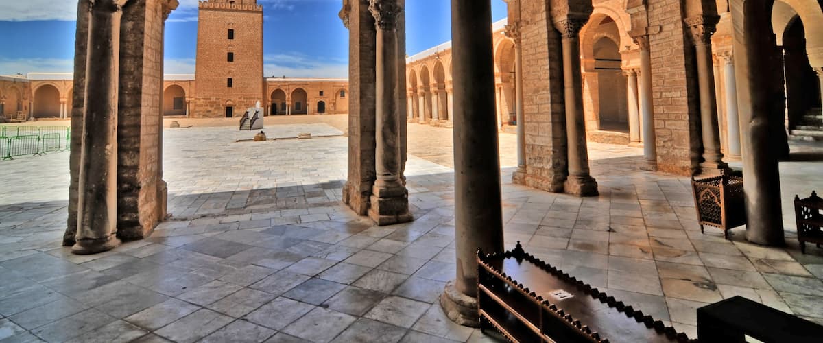 An ancient courtyard with arches, a tower, and a chessboard.