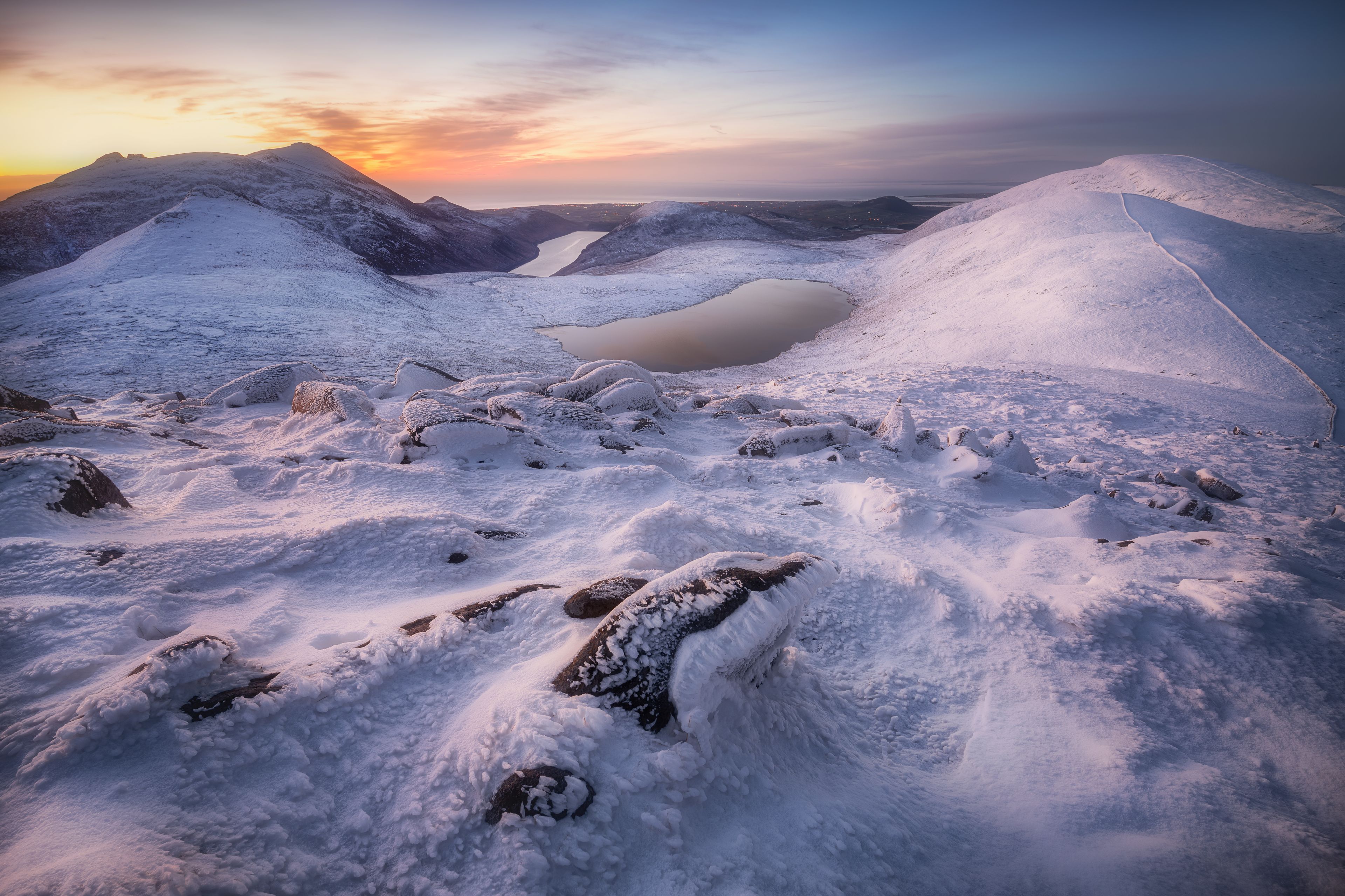 Paisaje montañoso nevado con un lago helado y rocas cubiertas de nieve.