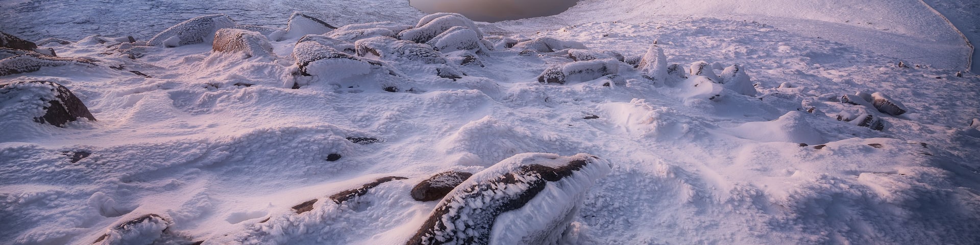 A snowy mountain landscape with a frozen lake and snow-covered rocks.