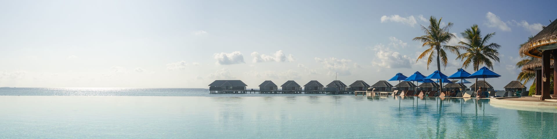A clear blue pool with overwater bungalows and palm trees.