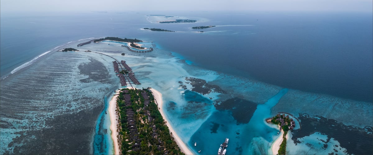 An aerial view of a coastal resort with a long sandy beach, clear turquoise waters, and several small islands.