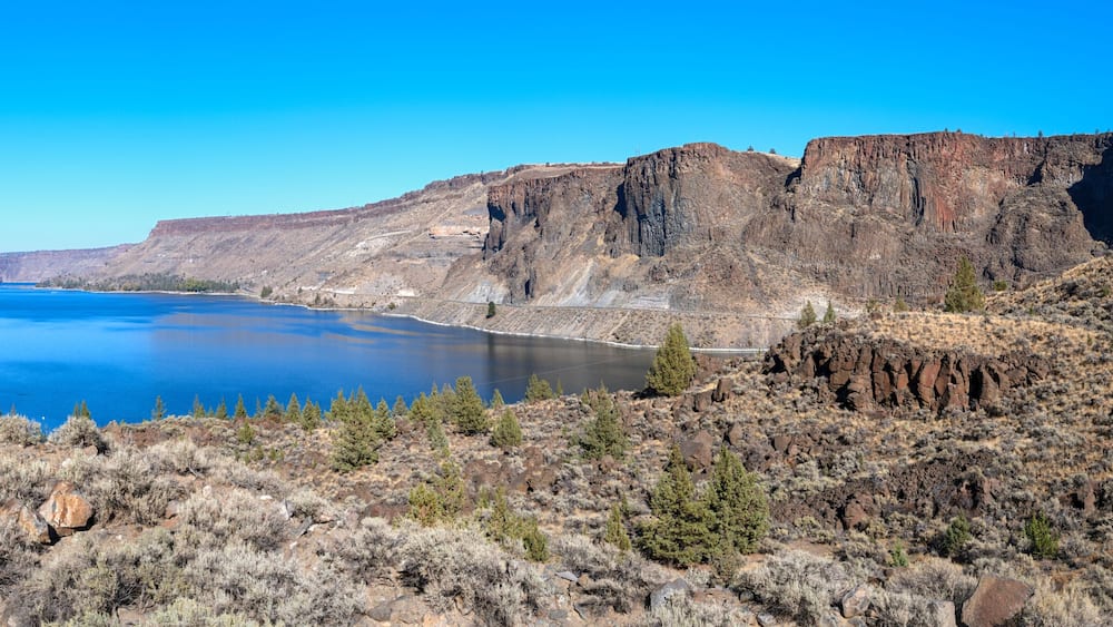 A canyon with a river, rocky cliffs, and sparse vegetation.