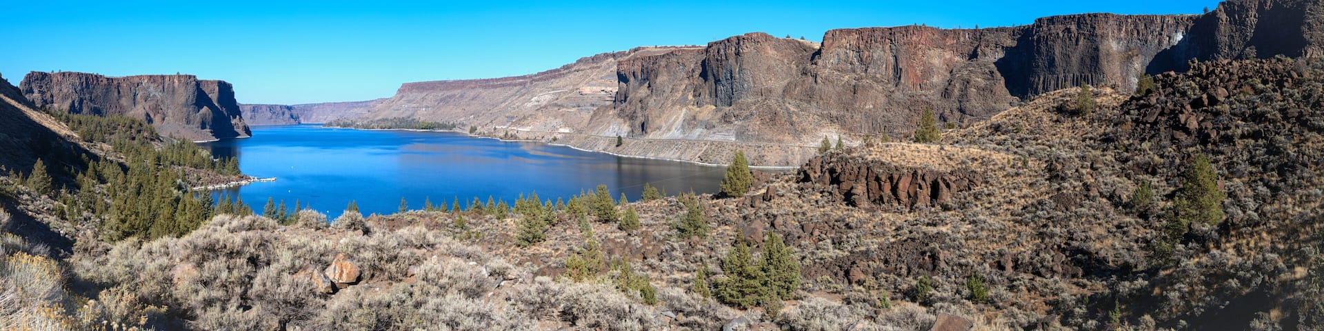 A canyon with a river, rocky cliffs, and sparse vegetation.