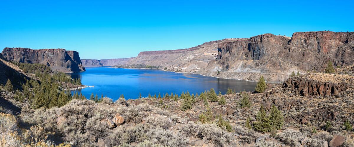 A canyon with a river, rocky cliffs, and sparse vegetation.