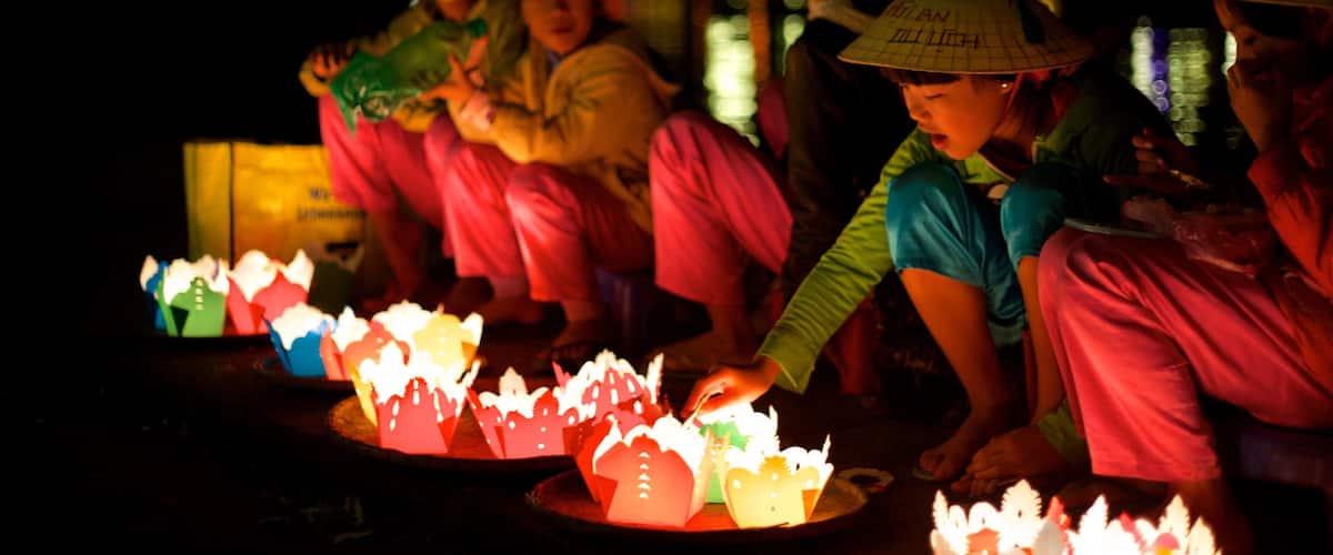 People wearing traditional hats and colorful clothing, sitting around a table with lit paper lanterns.