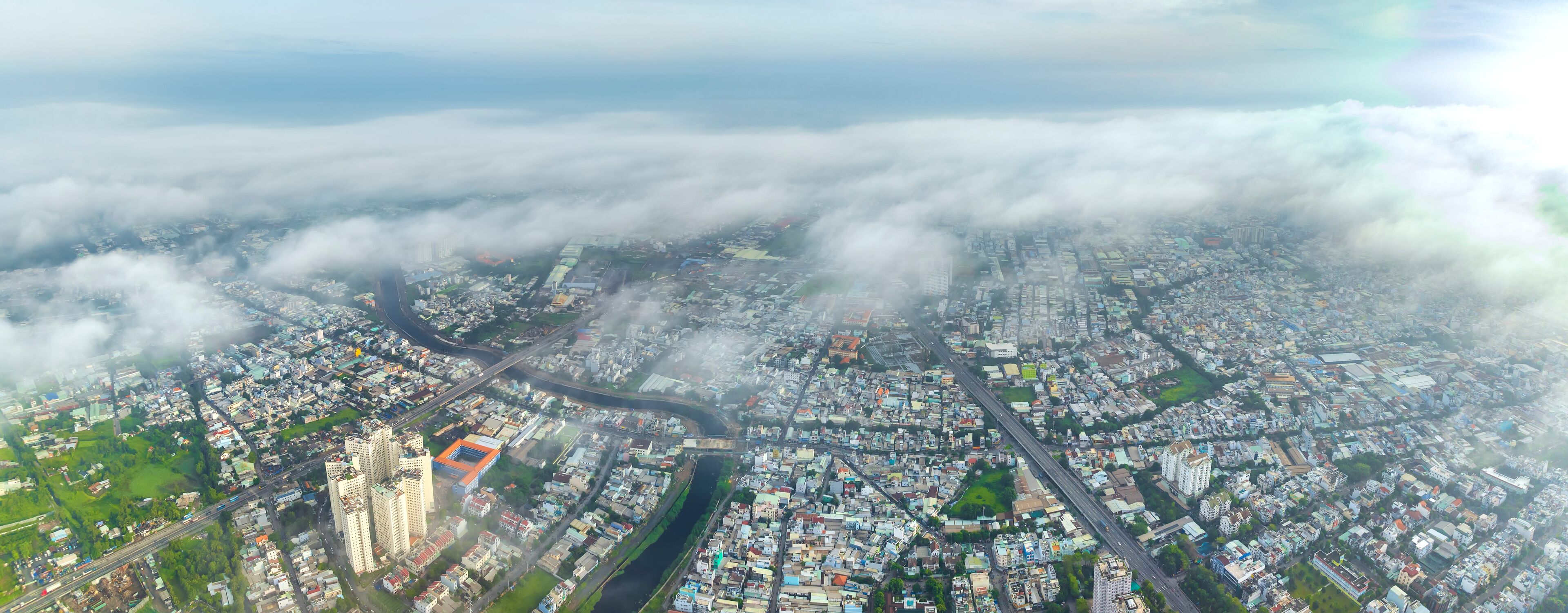 Vista aérea de uma cidade com intenso desenvolvimento urbano, um rio e áreas verdes ao redor.