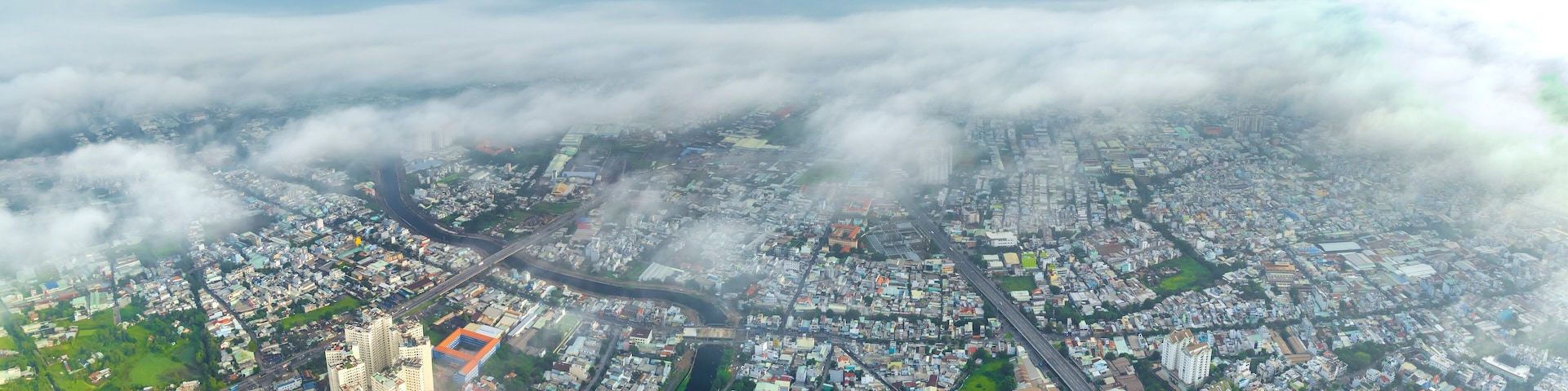 Vista aérea de uma cidade com intenso desenvolvimento urbano, um rio e áreas verdes ao redor.