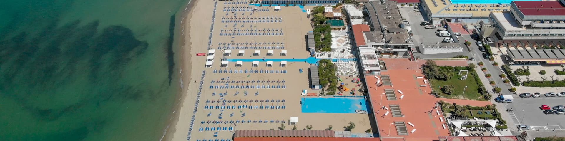An aerial view of a beach with rows of sun loungers and a swimming pool.